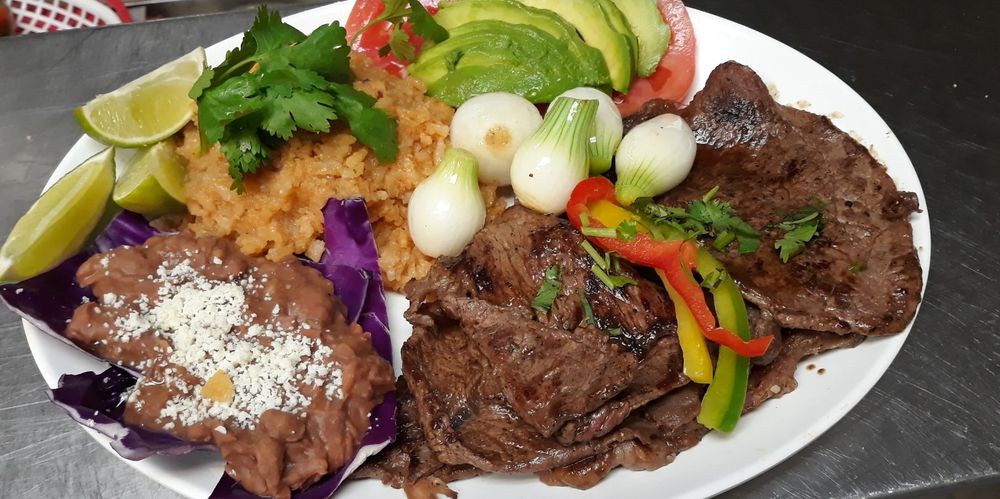 Carne asada plate with rice, refried beans, avocado, grilled onions and lime